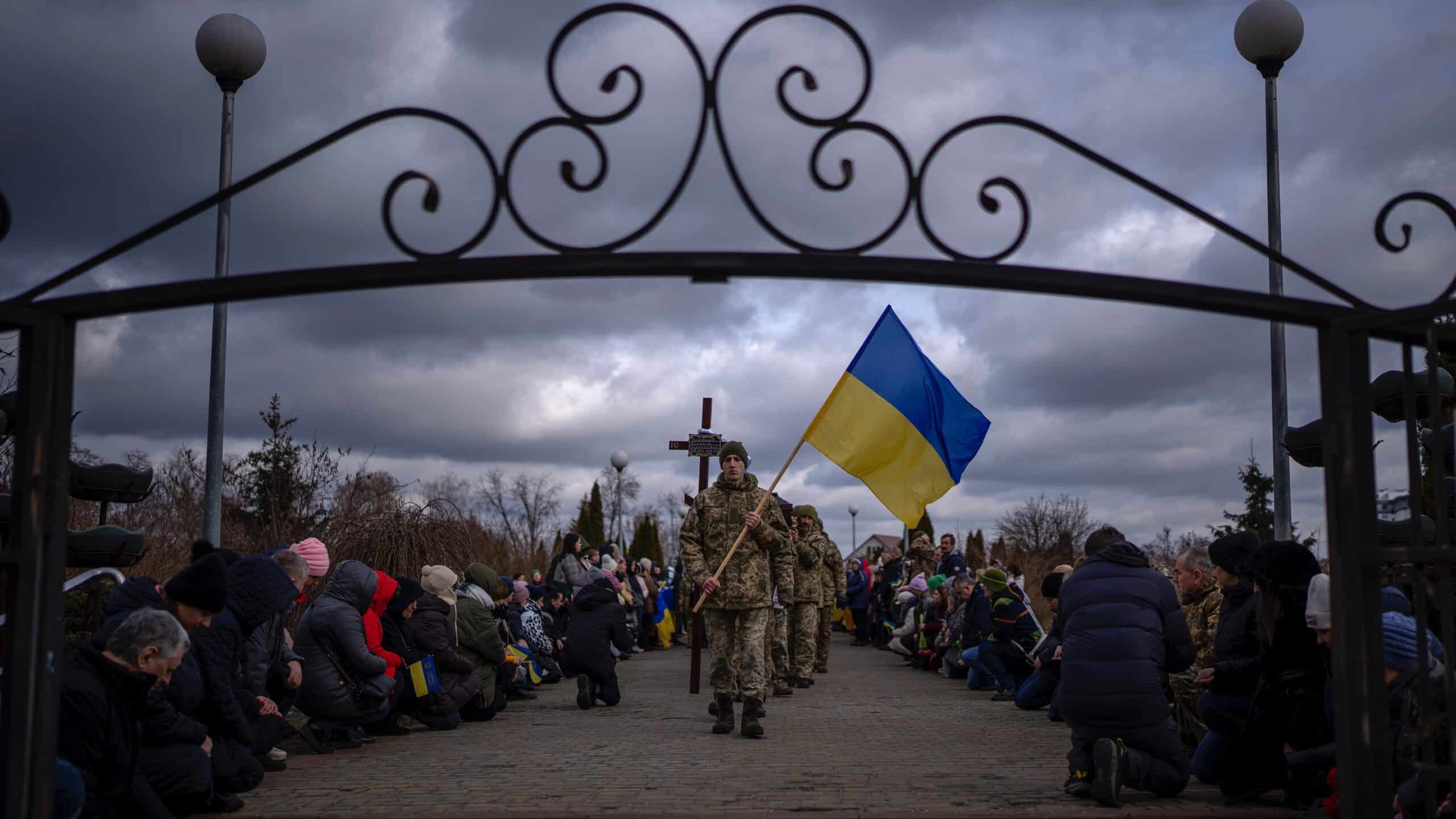 People in Brovary, Ukraine on Feb. 19, 2023 kneel at a funeral procession for the body of a man killed battle.