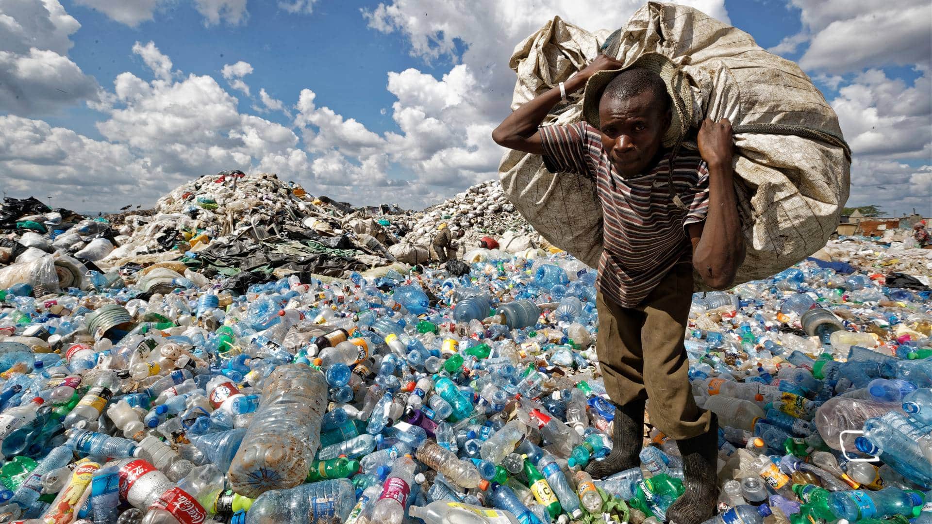 A man walks on a mountain of plastic bottles as he carries a sack of them to be sold for recycling after weighing them at the dump in the Dandora slum of Nairobi, Kenya 
