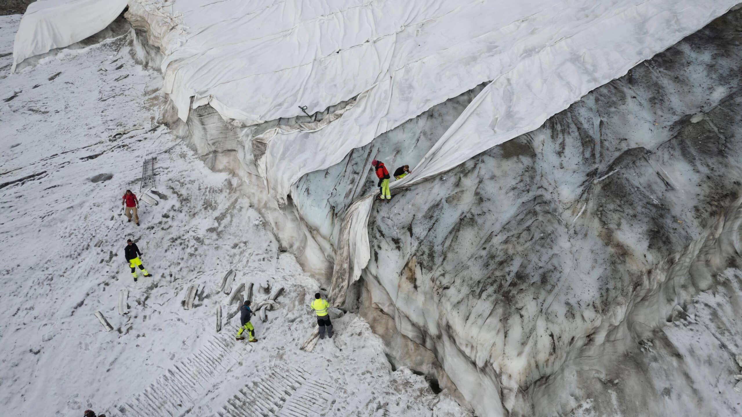 People work on a tarpaulin which cover the ice of the Corvatsch glacier.