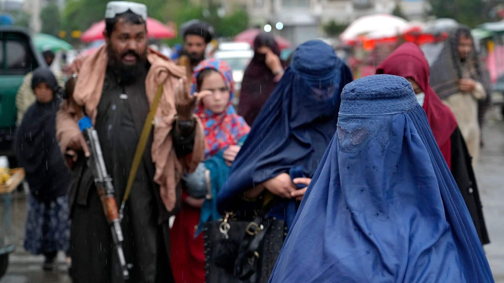 Afghan women walk through the old market as a Taliban fighter stands guard, in downtown Kabul, Afghanistan.